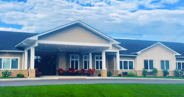 Front entrance of Autumn Trace Rensselaer Assisted Living with a covered walkway and red chairs.