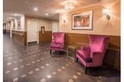 A well-lit interior hallway with two purple upholstered armchairs and a small side table beneath framed artwork.