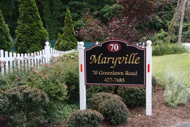 Maryville sign with address, surrounded by shrubs and a white picket fence.