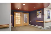 Interior hallway with double glass doors, handrails, bulletin board, and recessed ceiling lights.