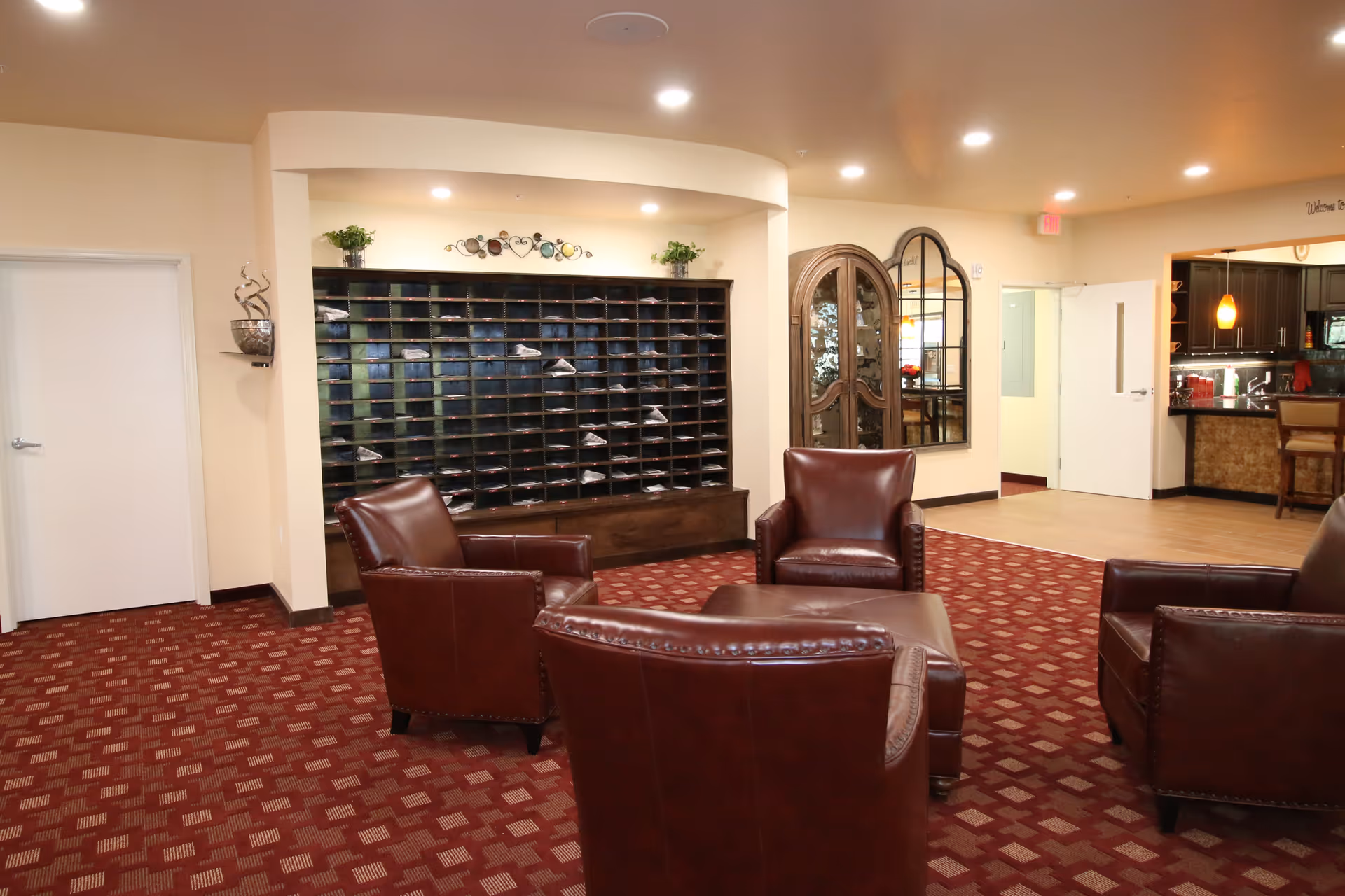 A senior living facility lounge with leather armchairs arranged around a central ottoman and a wall of mail cubbies.
