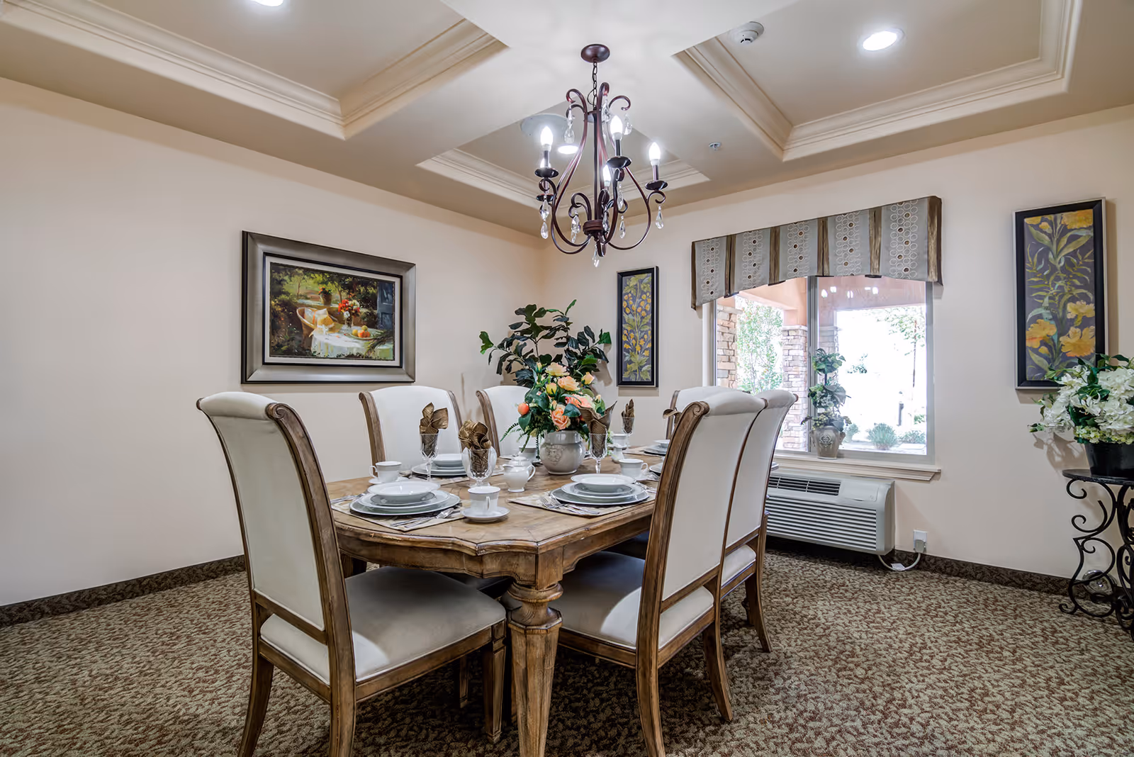 Elegant dining room with a set wooden table and upholstered chairs under a chandelier, artwork on the walls, and a window.