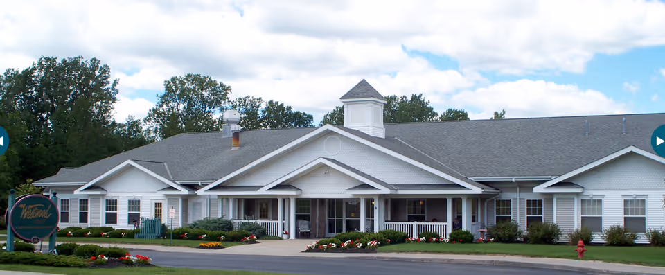 Front exterior of a single-story white senior living building with a covered entrance, landscaped lawn, and a sign reading 'Westwood'.