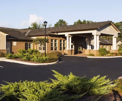 Exterior view of Stone Valley Assisted Living & Memory Care facility showing a single-story brick building with a covered entrance, surrounded by landscaped greenery and a paved driveway under a clear sky.