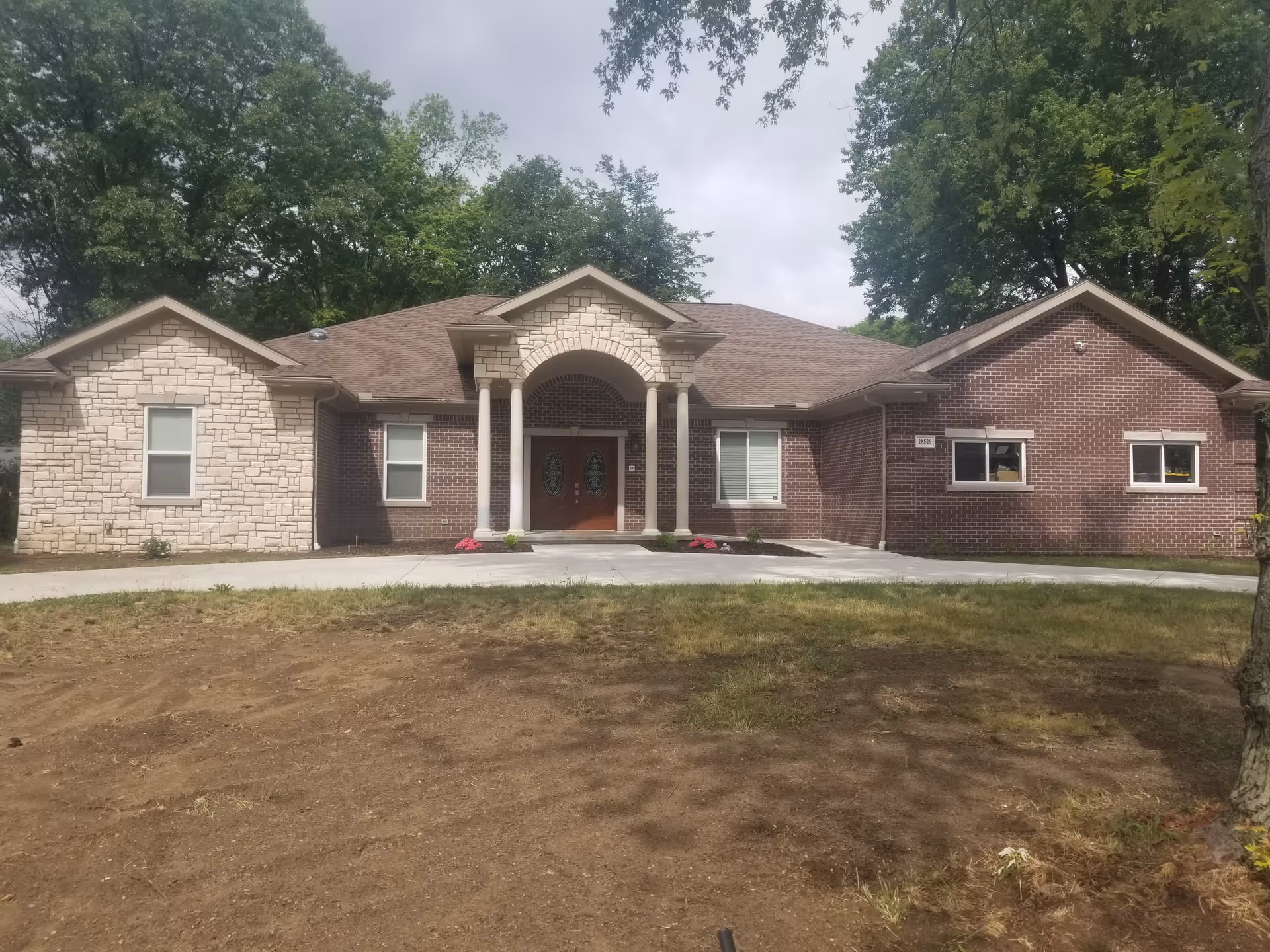 Front exterior of a single-story brick and stone building with a columned arched entrance and trees behind it.