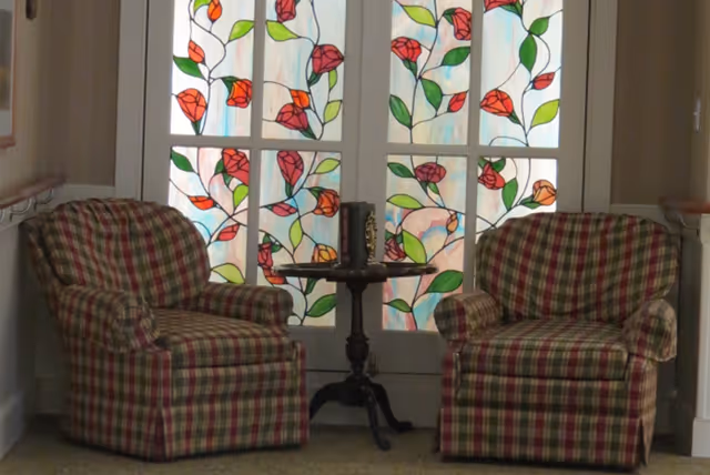 Two plaid armchairs flank a small round table in front of decorative stained-glass doors.