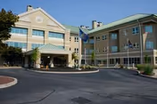 Front entrance of a multi-story veterans center building with a circular driveway, flagpoles, and landscaped beds under a clear blue sky.