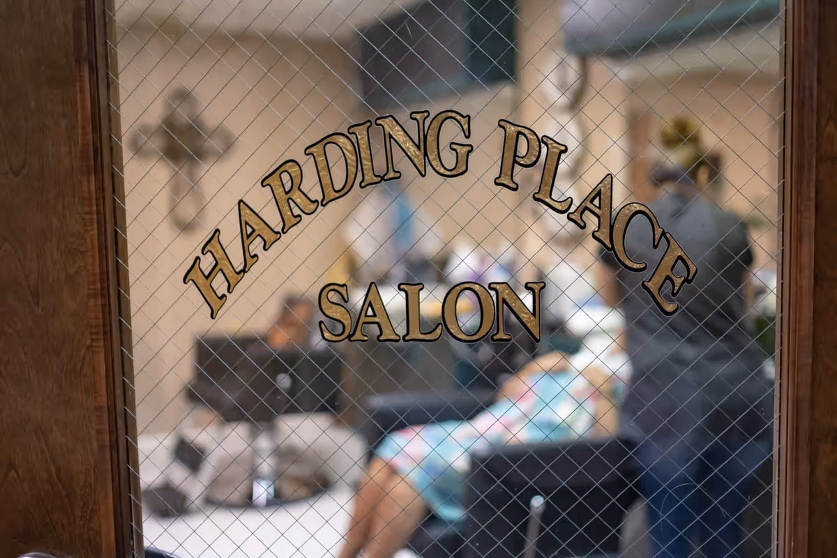 View through a wired-glass door reading "Harding Place Salon" into a salon with a stylist and a seated client blurred inside.