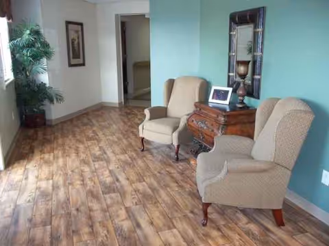 A cozy senior living room featuring two beige armchairs, a wooden dresser, and a wall mirror.