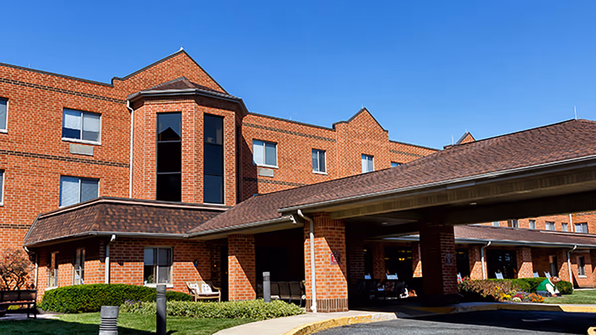 Exterior view of a multi-story brick building with a covered entrance and well-maintained landscaping under a clear blue sky.