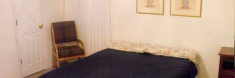 A small bedroom with a bed, chair, door, and framed pictures on the wall.