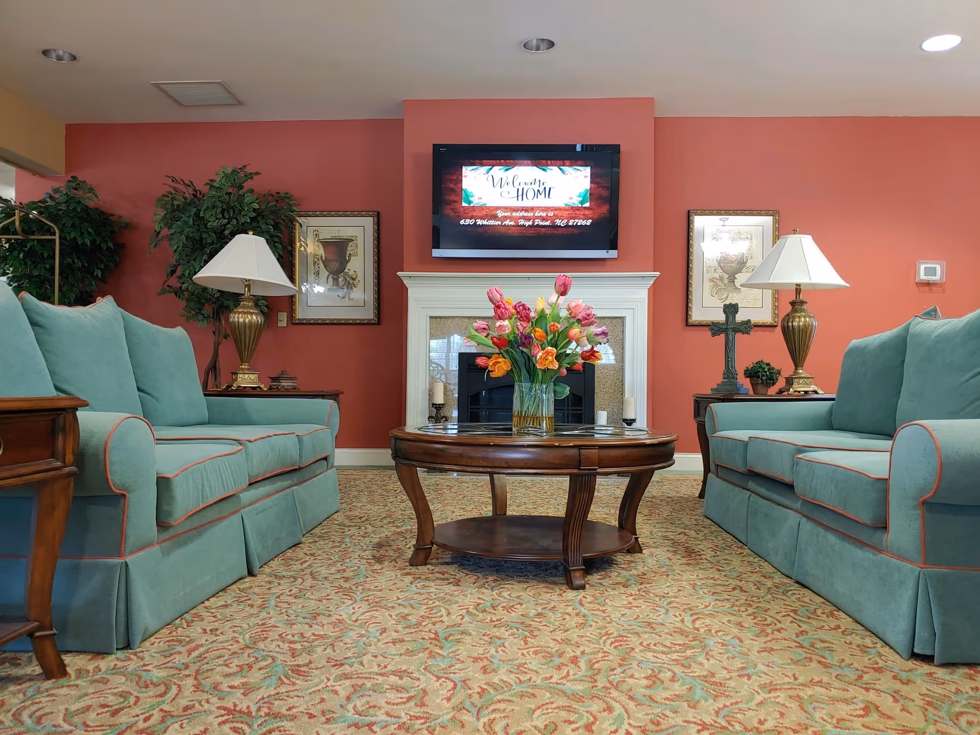 Living room seating area with teal sofas, a fireplace, TV, and floral centerpiece.