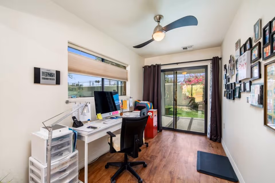 Home office with a desk, computer, rolling chair, gallery wall, and sliding glass door leading to a small yard.