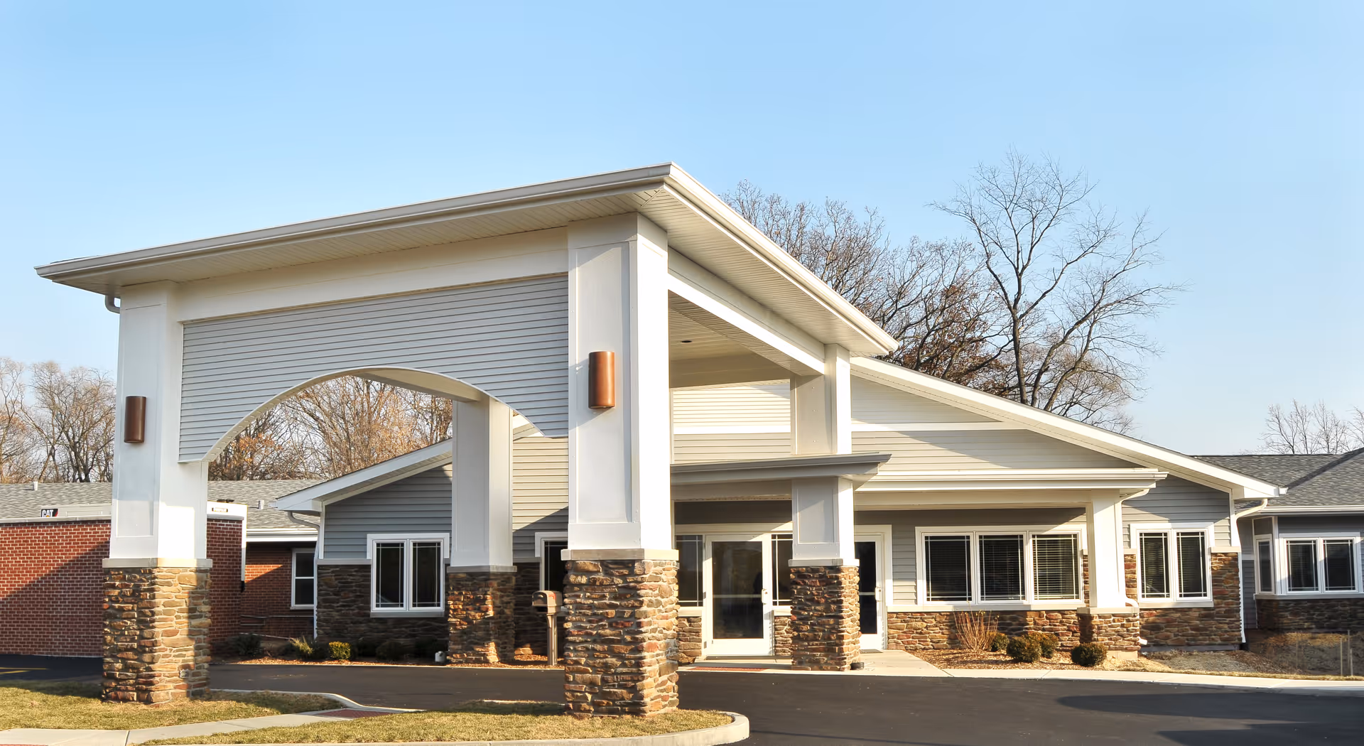 Front exterior view of Fair Oaks Health Care Center building with a covered entrance supported by stone pillars, multiple windows, and a clear sky in the background.