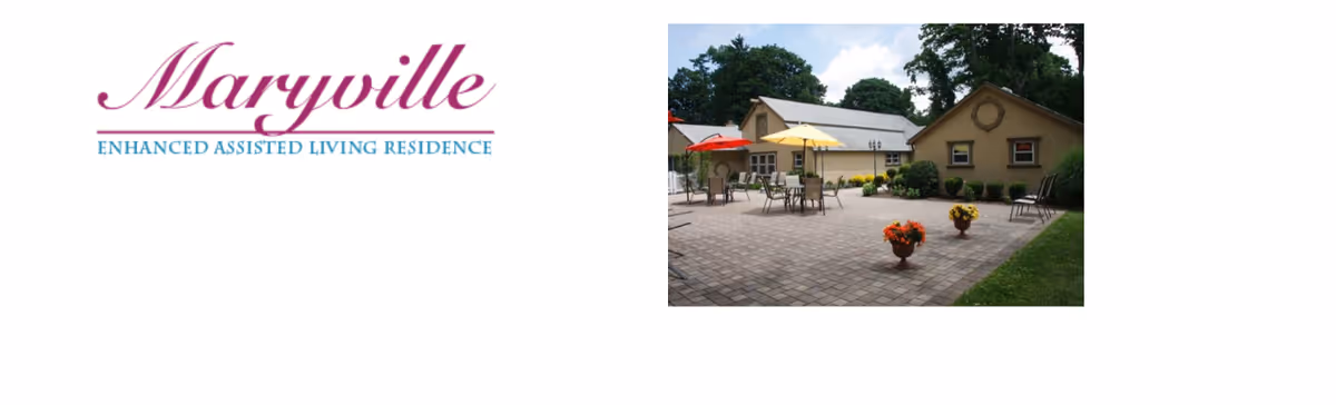 Outdoor patio area of Maryville Enhanced Assisted Living Residence with tables, chairs, and umbrellas surrounded by a garden and trees.