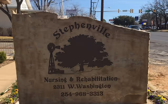 Stone entrance sign reading 'Stephenville Nursing & Rehabilitation' with the address and phone number, positioned by a sidewalk and street.