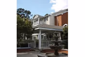 Exterior view of a multi-story brick senior living building with a covered columned entrance, balcony, and a fountain in the foreground.