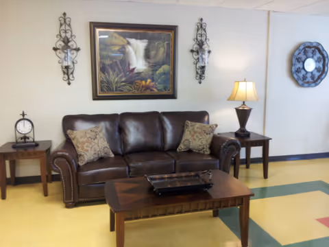 Cozy lounge area with a brown leather sofa, coffee table, lamps, and wall art.