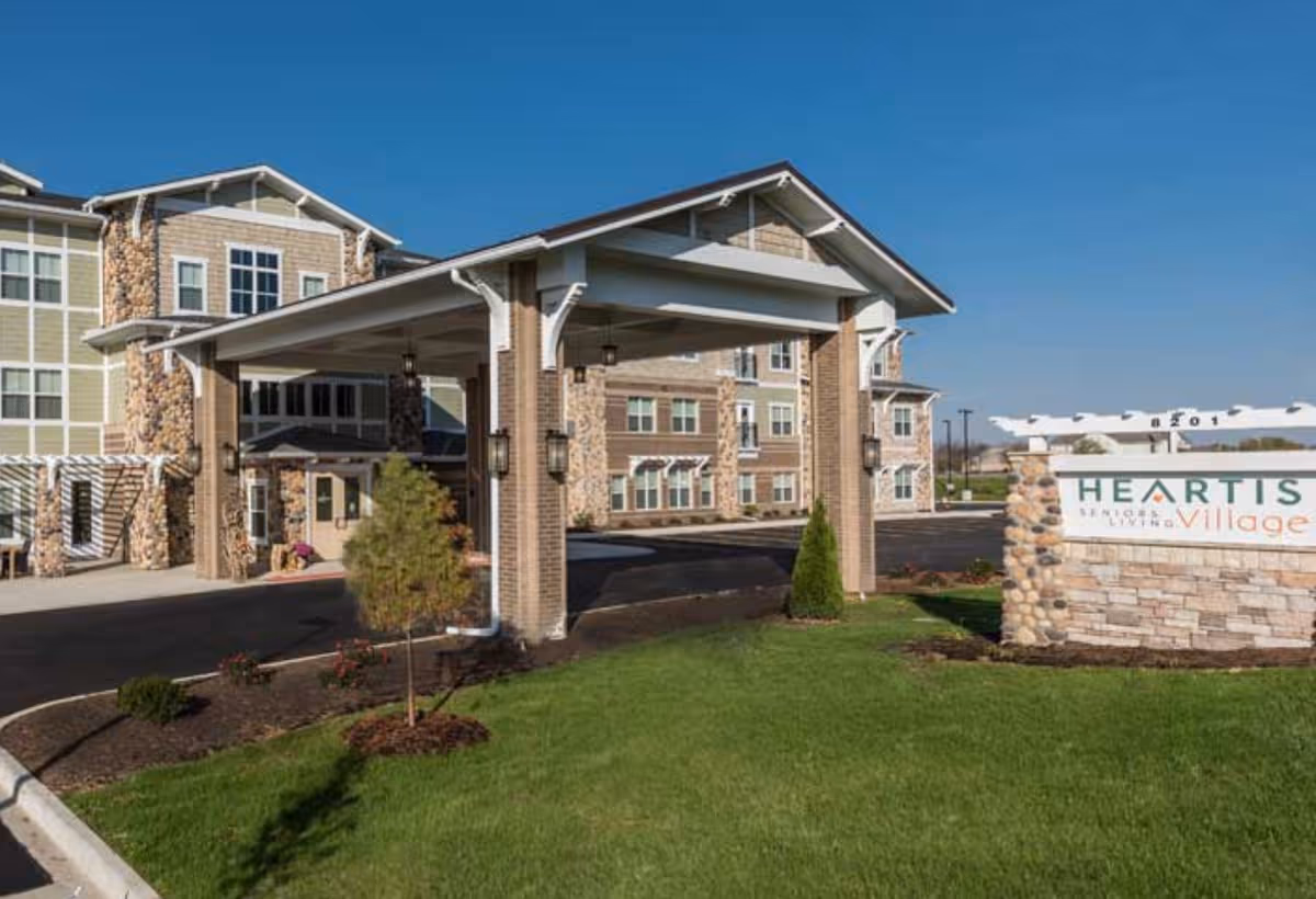 Exterior view of Heartis Village senior living entrance with sign and brick facade.