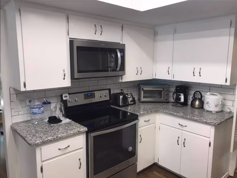 Bright white kitchen with granite countertops and stainless steel appliances.