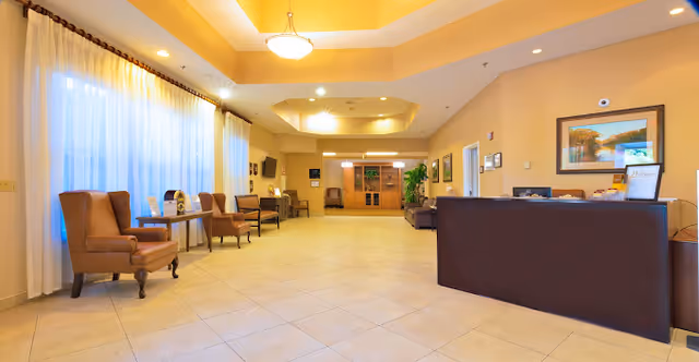 Spacious, well-lit senior living facility lobby with a reception desk, seating areas, and tiled floor.