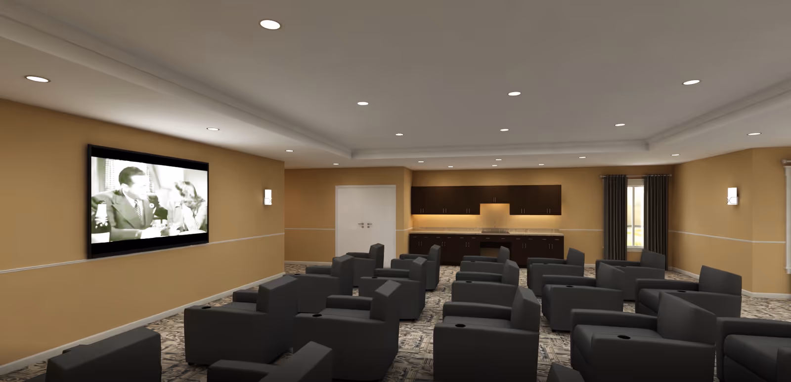 A senior living media room with rows of gray armchairs facing a wall-mounted TV and a kitchenette at the back.