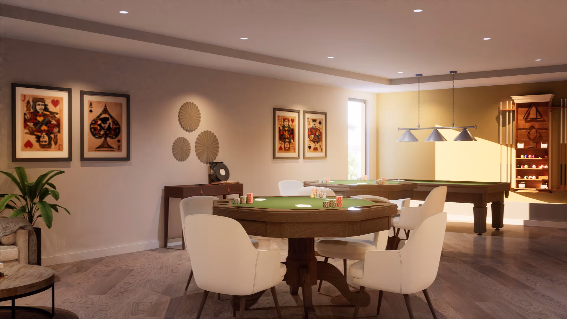 A well-lit game room with a poker table surrounded by four white chairs, a pool table in the background, and framed playing card artwork on the walls. There is a plant in the corner and a wooden cabinet holding pool cues and billiard balls.