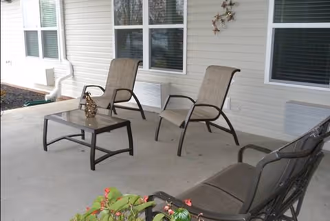 Outdoor patio with lounge chairs and a glass table against a beige facility wall.