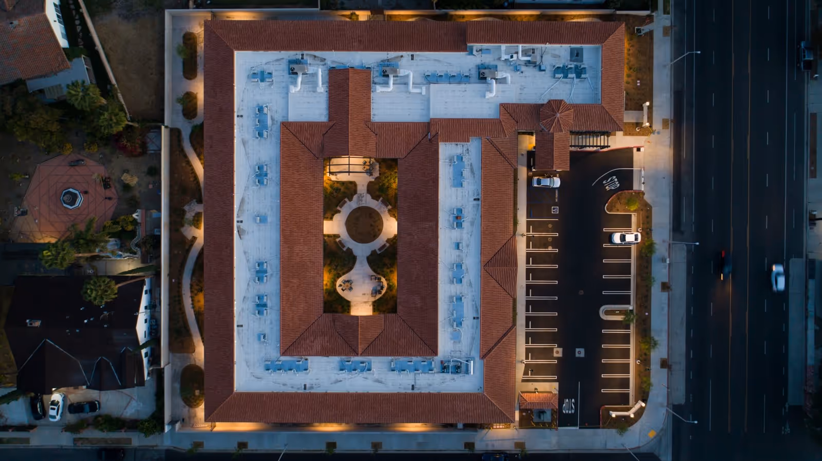 Aerial nighttime view of The Preserve at Woodland Hills Assisted Living & Memory Care building with a central courtyard, surrounding parking lot, and adjacent streets illuminated by streetlights.