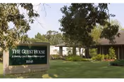 Front exterior view of The Guest House sign with lawn, trees, and building entrance.