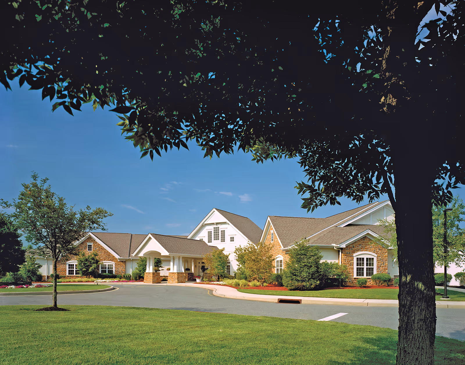 Brick senior living facility with a curved driveway, green lawn, and trees.