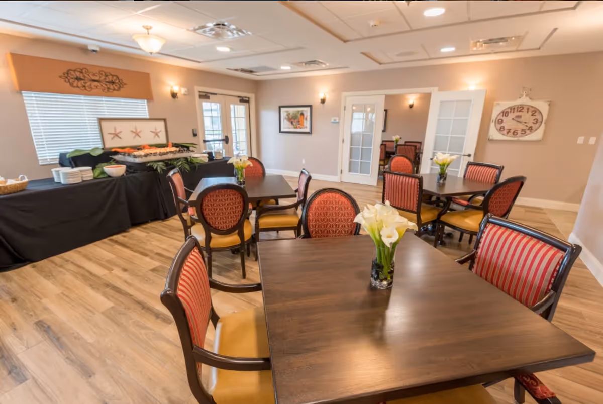 Dining room with several wooden tables and red-striped upholstered chairs, each table adorned with a small vase of white flowers.