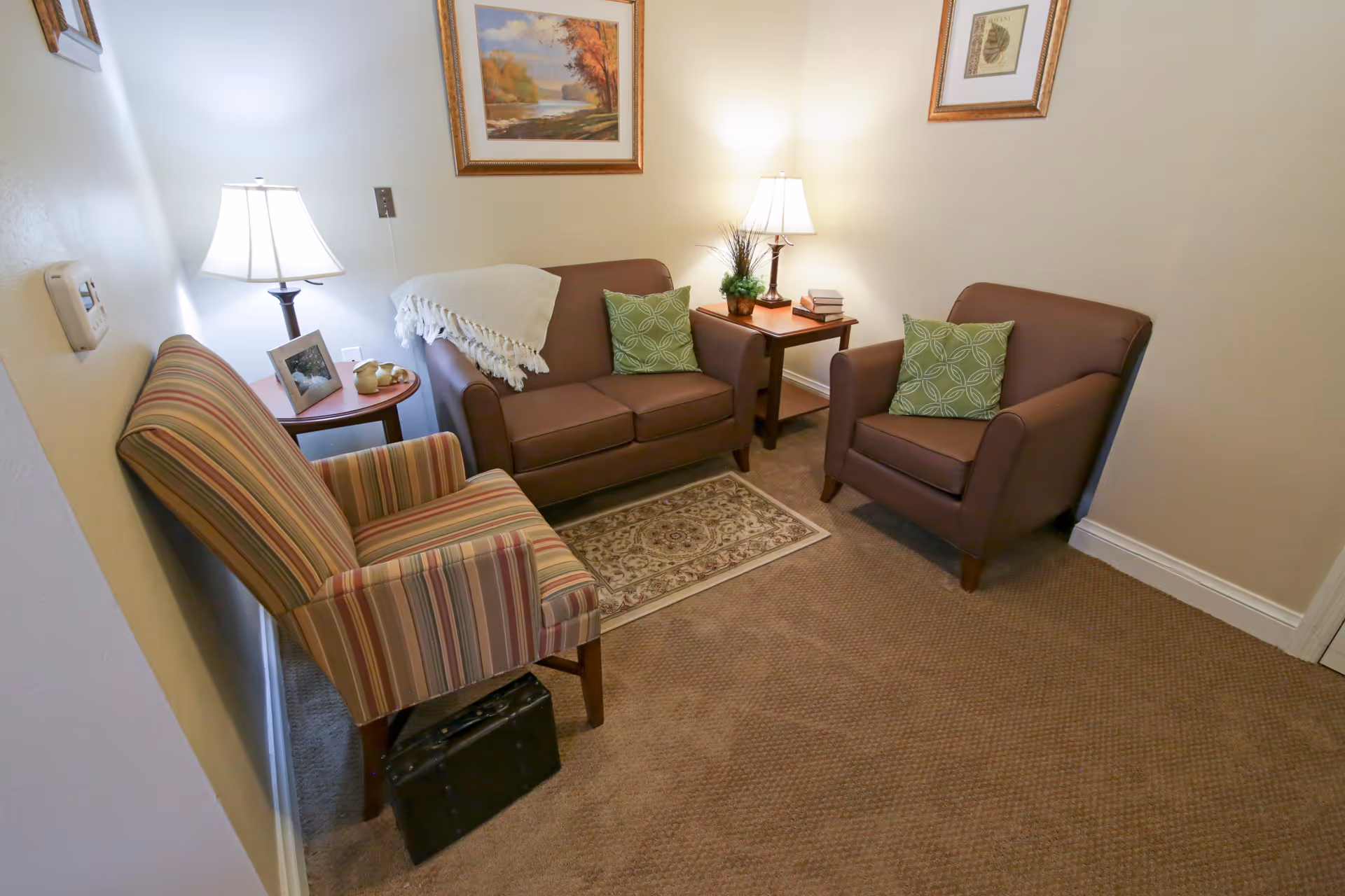 Cozy sitting area with a loveseat, two armchairs, side tables with lamps and framed artwork on the walls.