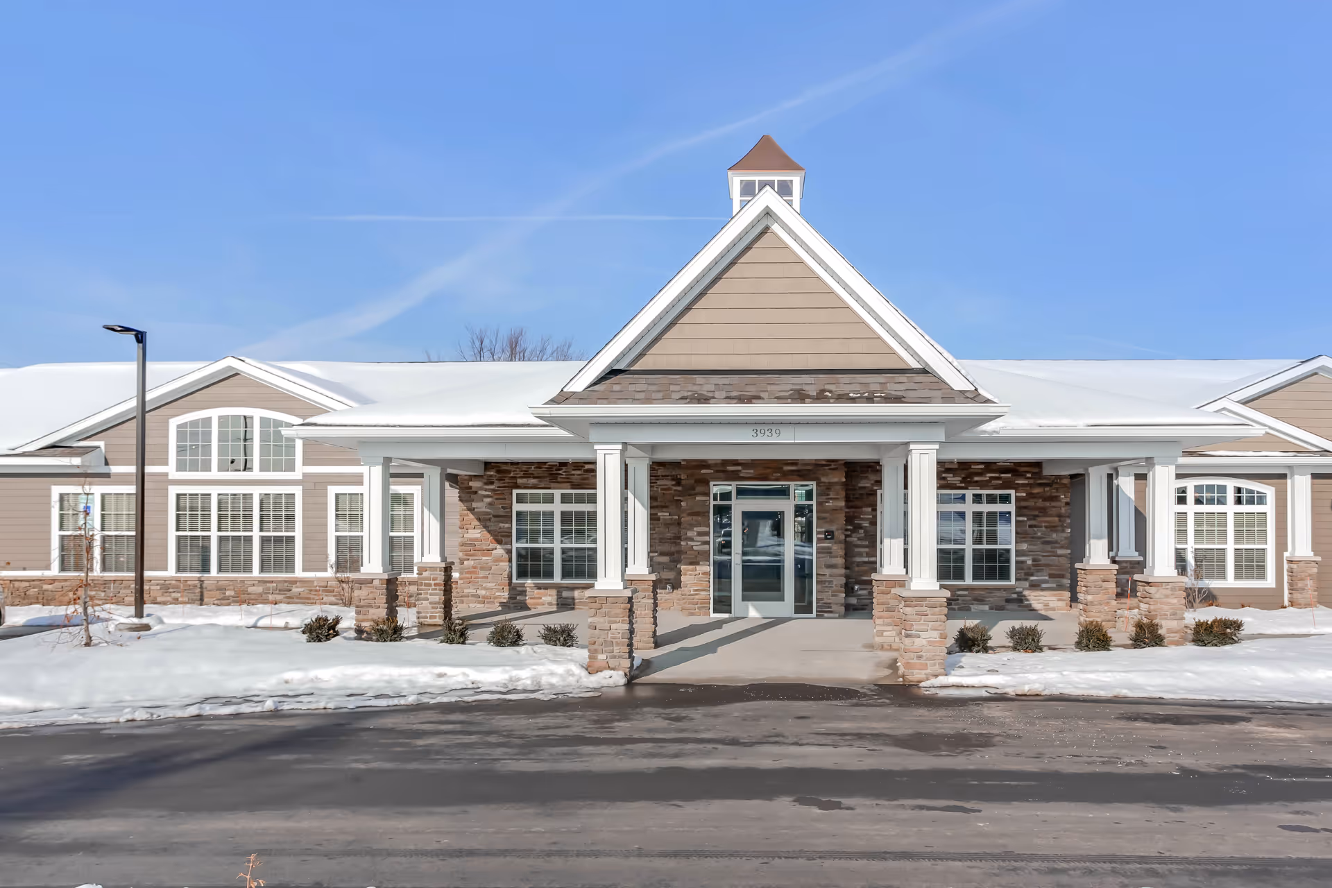 Front entrance of a single-story assisted living building with brick and siding facade, a covered portico, and snow on the ground.