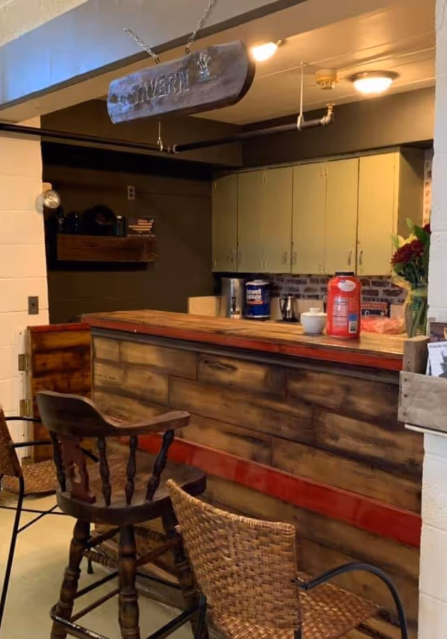 Wooden tavern-style indoor bar with high chairs, a countertop and cabinets in a common area.