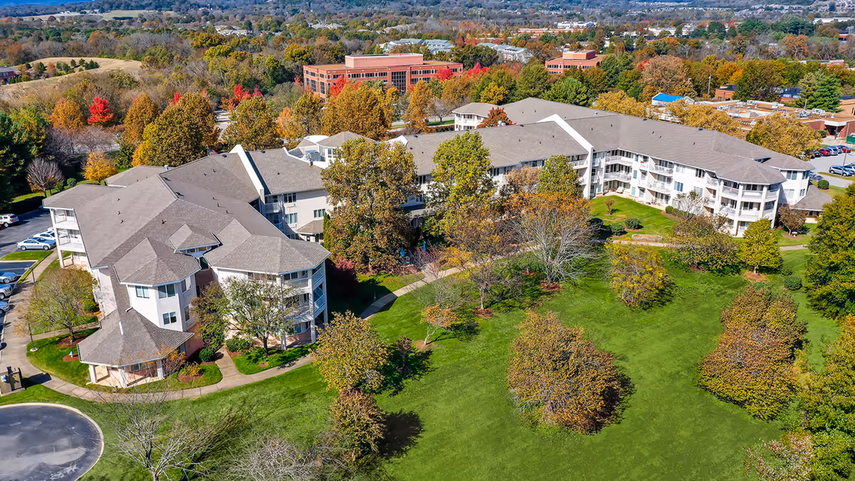 Aerial view of a large multi-story senior living complex surrounded by green lawns and trees with autumn foliage.
