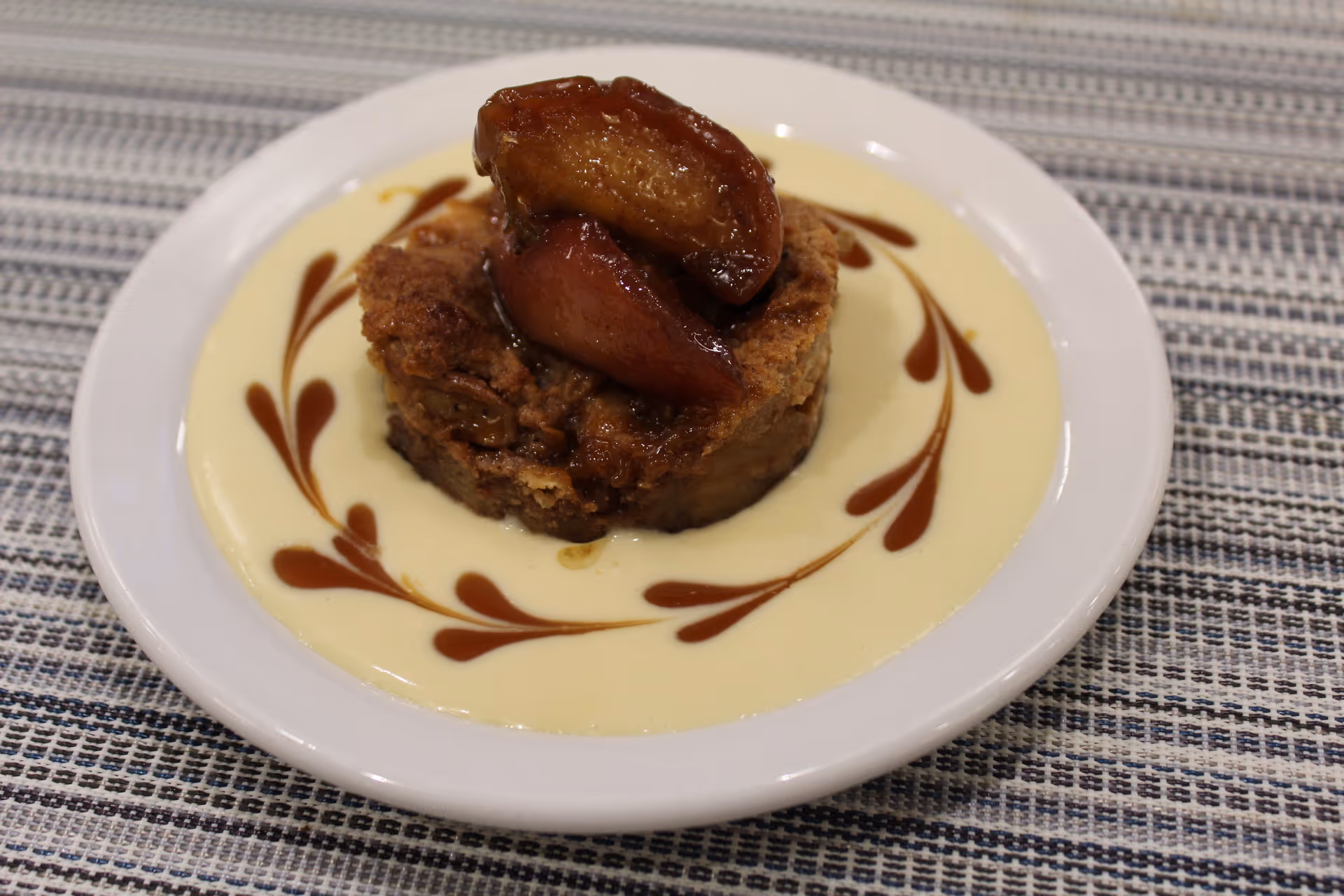 A plated bread pudding topped with caramelized fruit served in a pool of custard with caramel decorative swirls.