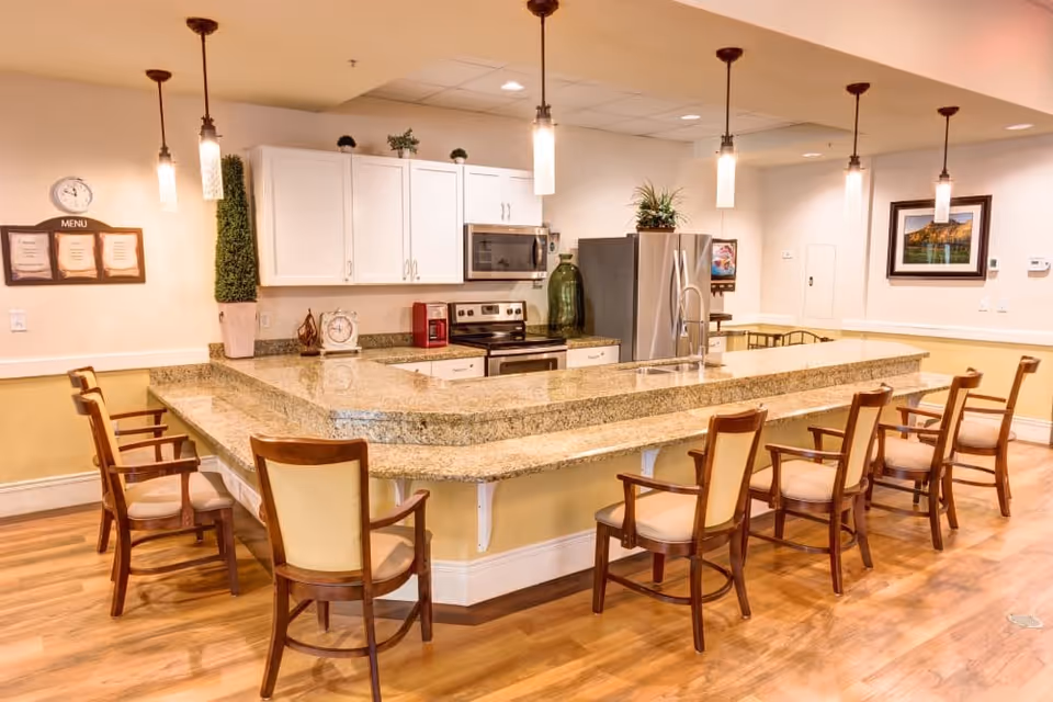 Spacious communal kitchen and dining area with a large granite island surrounded by wooden chairs and pendant lights.