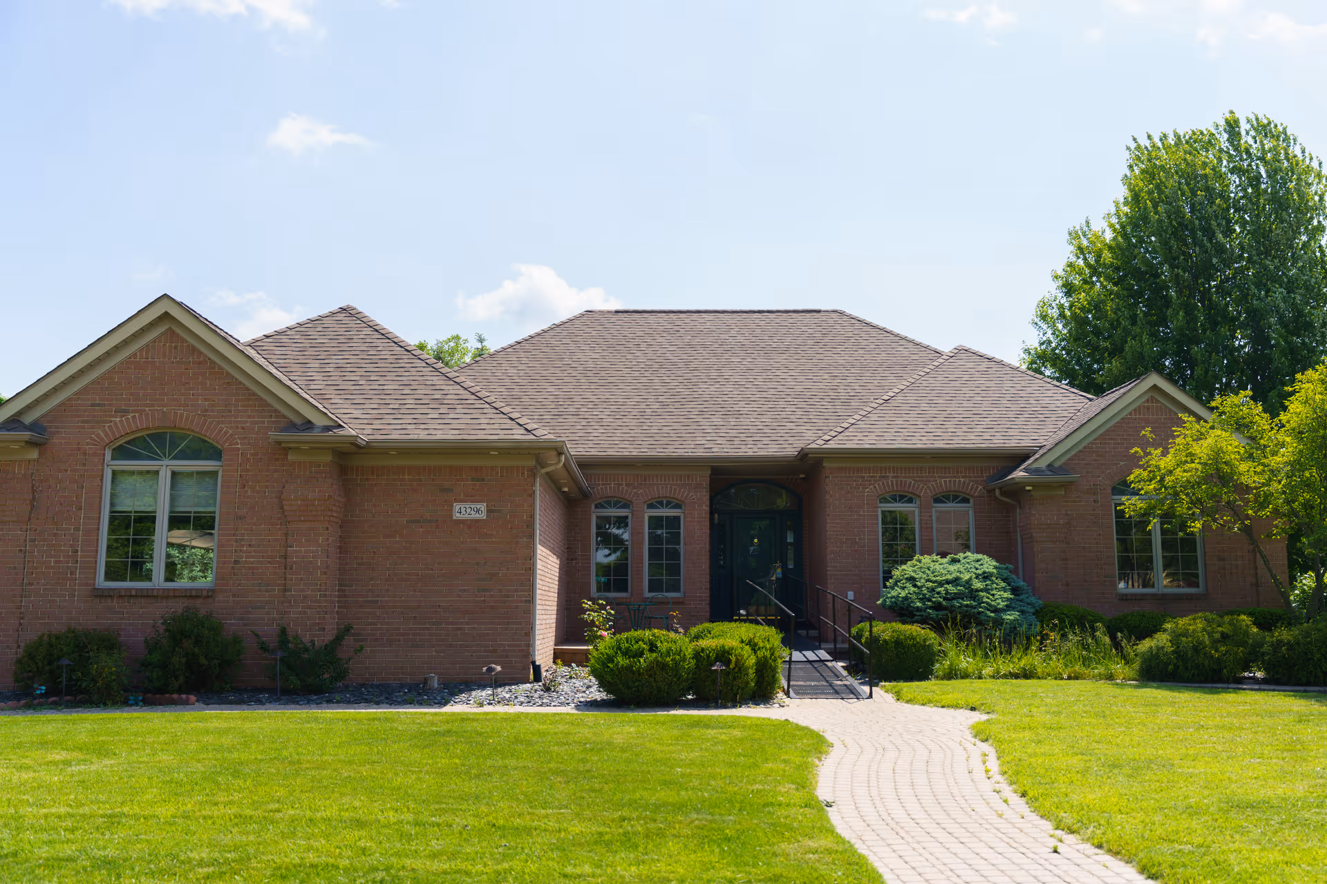 Single-story brick building with a central entrance, landscaped shrubs and a curved brick walkway across a lawn.
