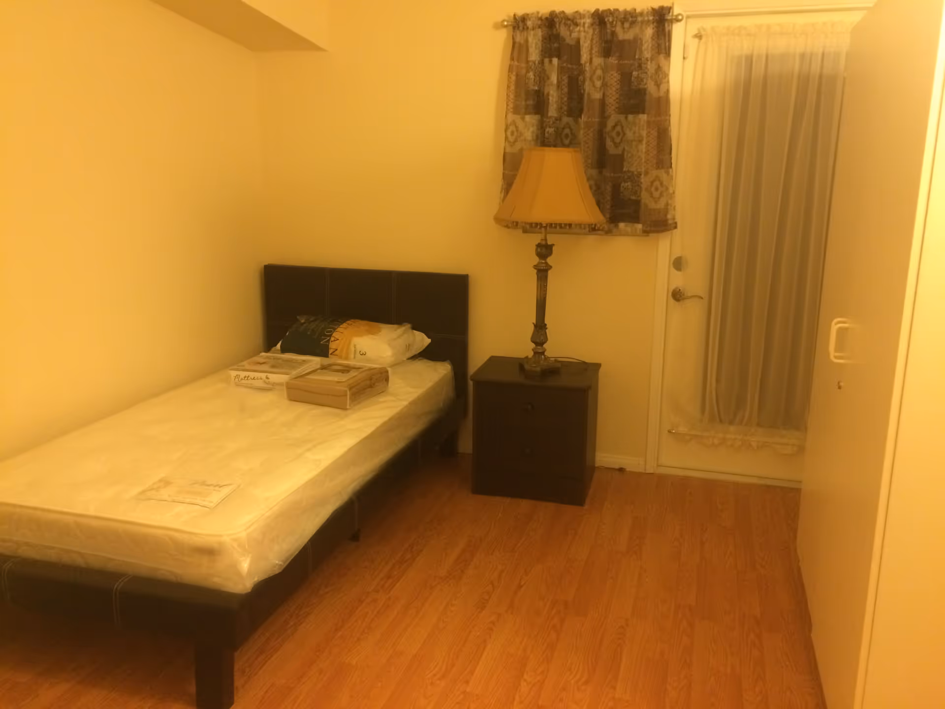 Small bedroom with a single bed, nightstand, lamp, and a curtained door.