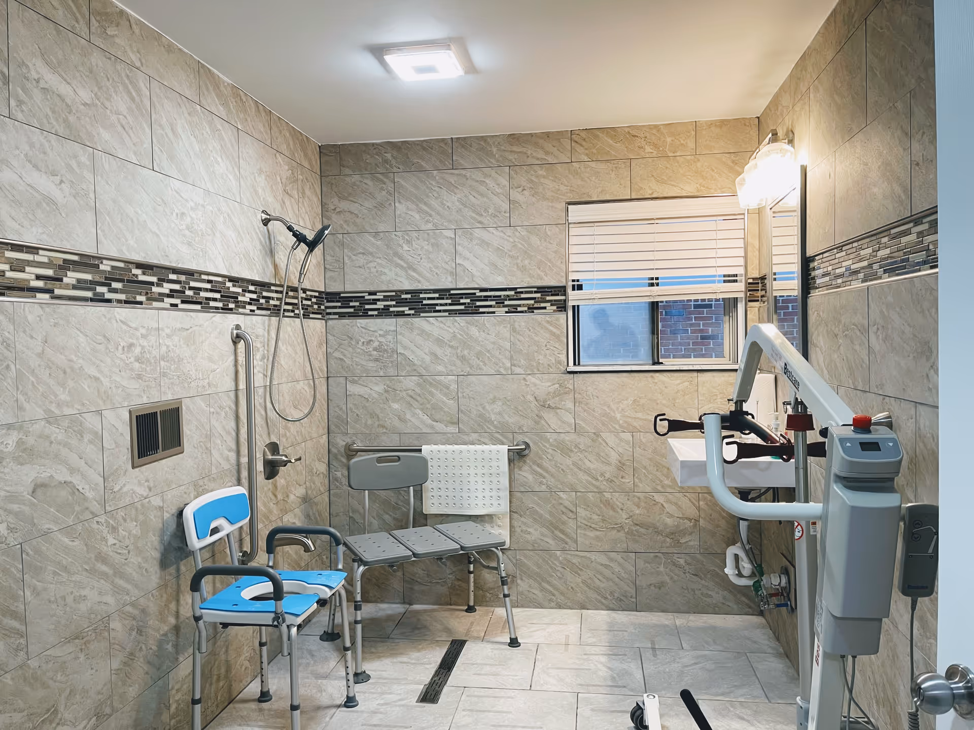 A tiled bathroom in a senior facility with a shower, seating, and accessibility aids.