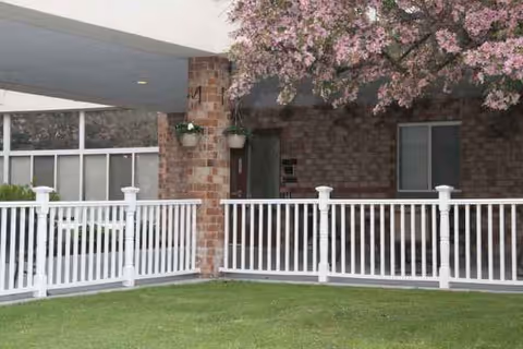 Exterior view of Absolut Care of Westfield featuring a brick entrance, white railing, and blooming tree.