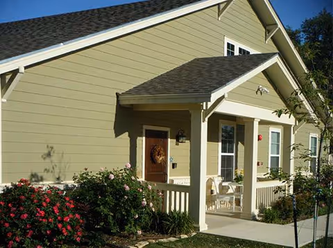 Exterior view of a beige senior living facility with a front porch and seating.