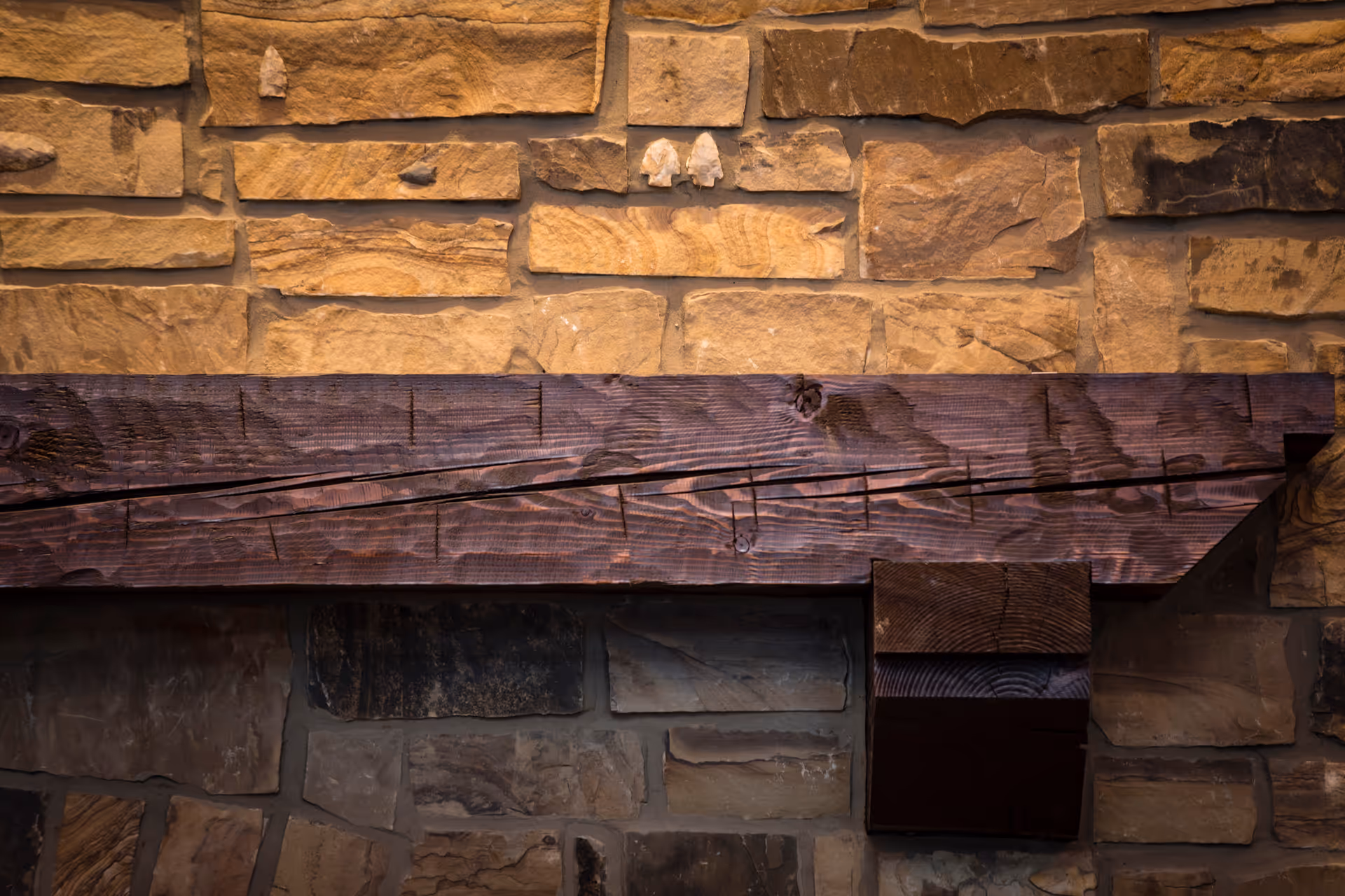 Close-up view of a rustic stone wall with a dark wooden beam mounted horizontally across it.