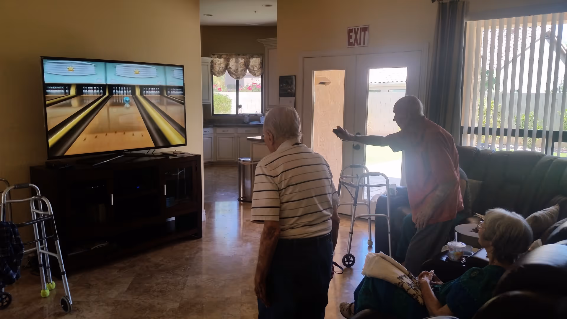 Residents in a living room area using a motion-controlled bowling game shown on a large TV.
