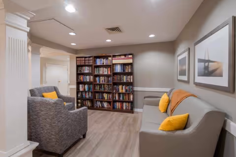 Communal lounge with a sofa, armchair, and bookshelves against a neutral-toned wall.