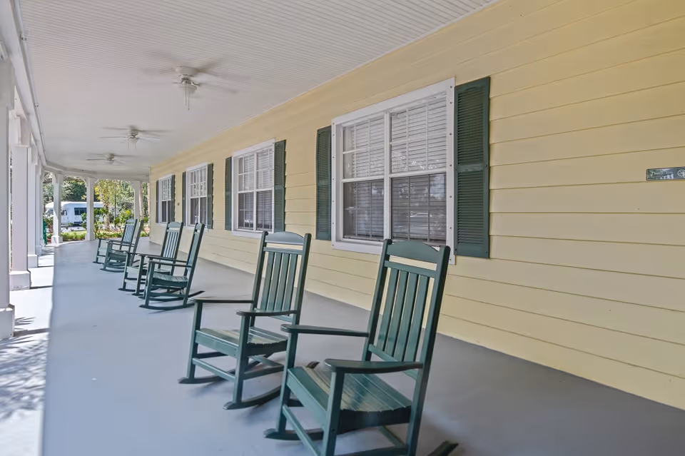Covered front porch with a row of green rocking chairs along a yellow-sided building.