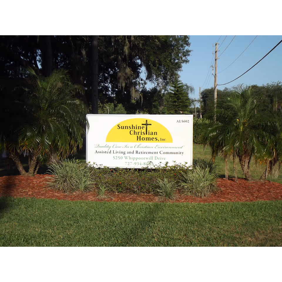 A landscaped entrance sign reading "Sunshine Christian Homes, Inc." set among palm trees and grass.