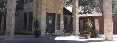 Stone building exterior with columned entry, glass doors, and potted plants near the entrance