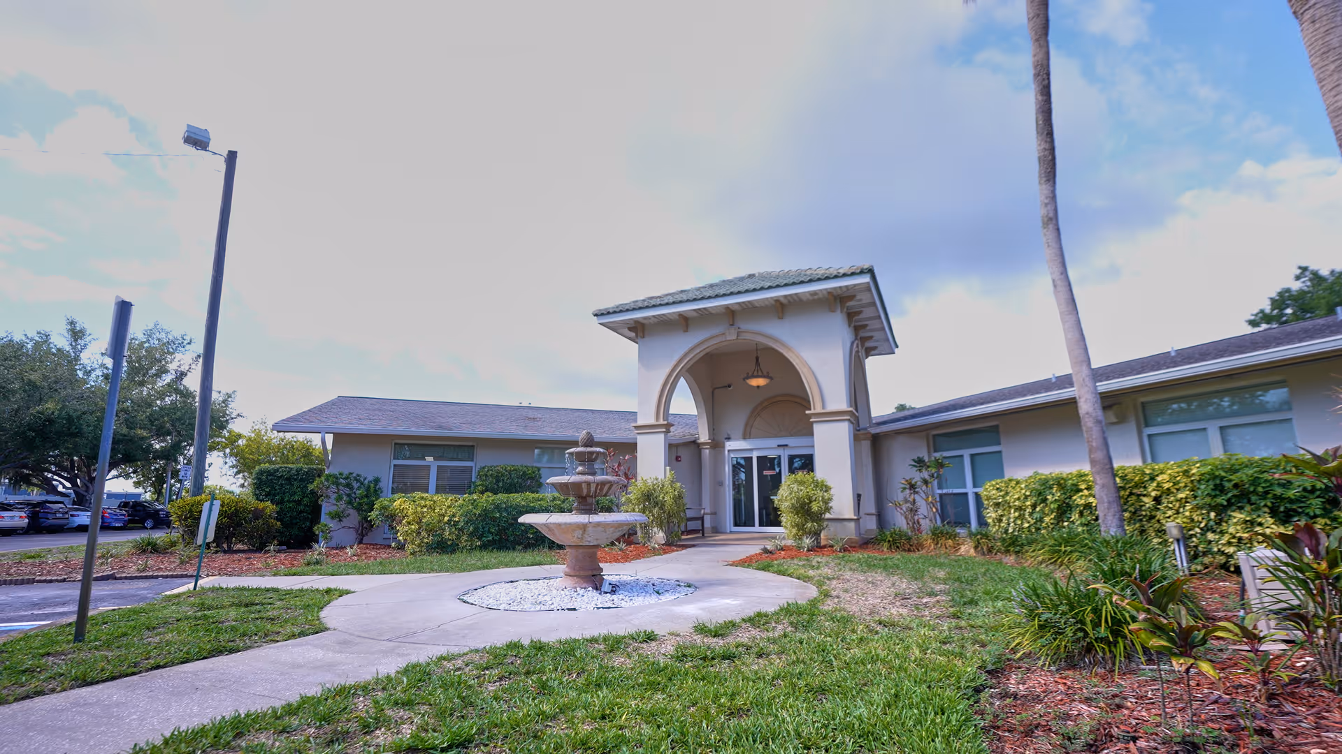 Front entrance of a single-story rehabilitation and nursing center with a covered portico, central fountain, walkway, and landscaped grounds.